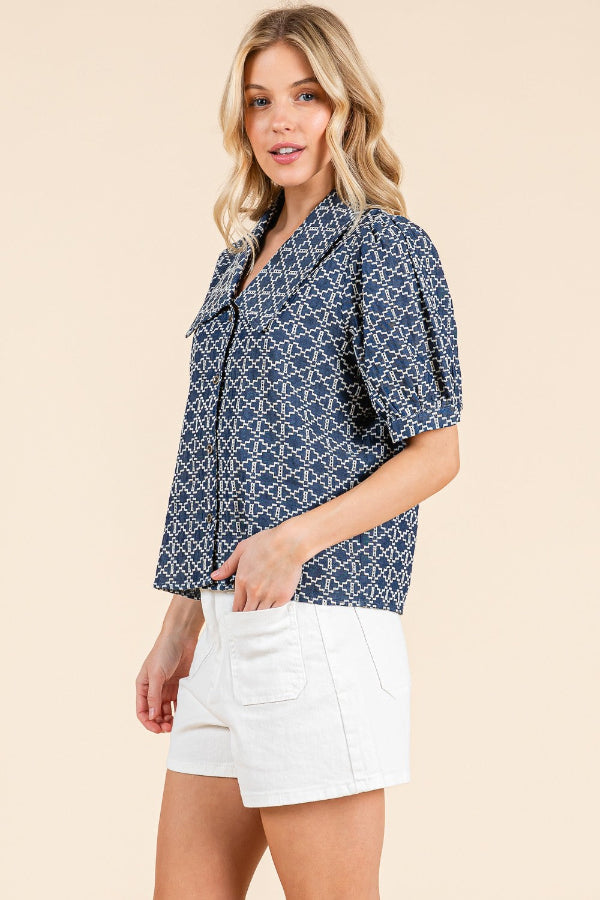 Woman wearing a blue patterned top and white shorts on a beige background
