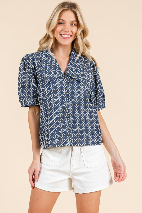Woman wearing a blue patterned shirt and white shorts on a beige background